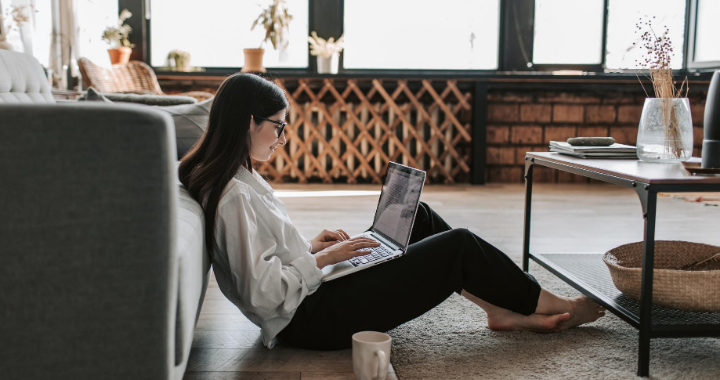 A woman using Microsoft Teams on her laptop while sitting on the floor. 